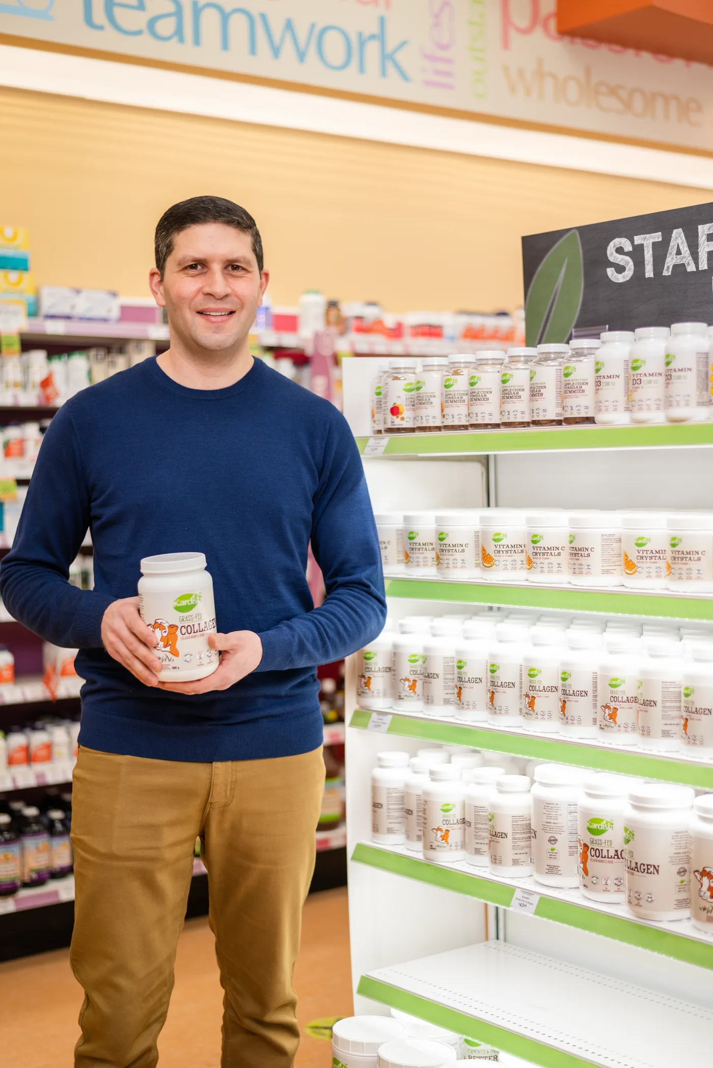 Robert Assaf holding Kardish private label collagen in front of a shelf of Kardish-brand products